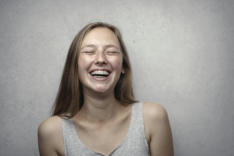 a woman is laughing with her eyes closed, by Attila Meszlenyi, pexels contest winner, hyperrealism, plain background, young teen, both laughing, underbite