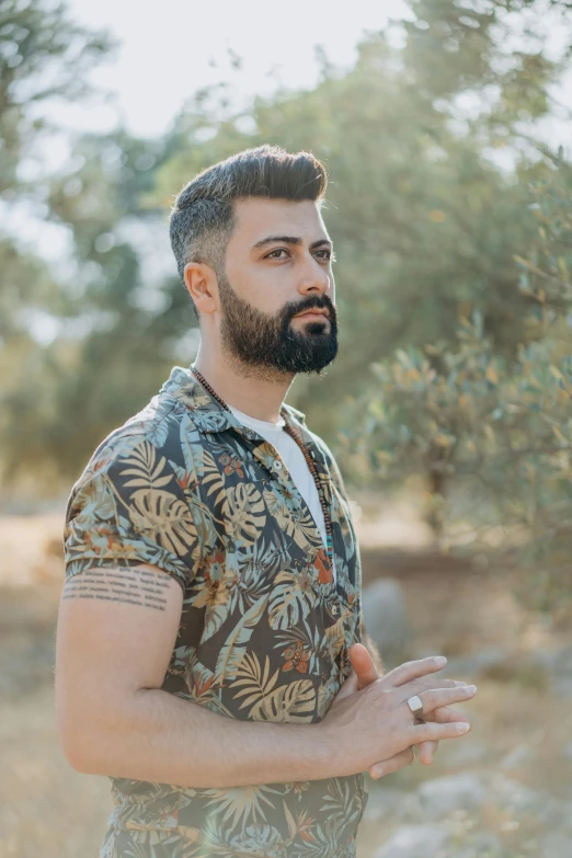 a man with a beard standing in a field, inspired by Nadim Karam, trending on reddit, undercut hairstyle, 2019 trending photo, olive skin color, tropical