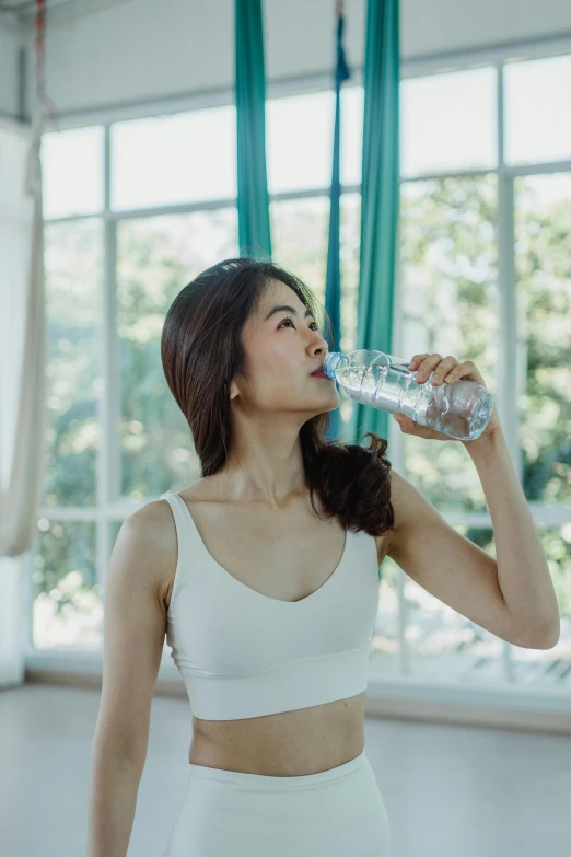 a woman in a white sports bra top drinking water, asian features, with backdrop of natural light, over it's head, profile image