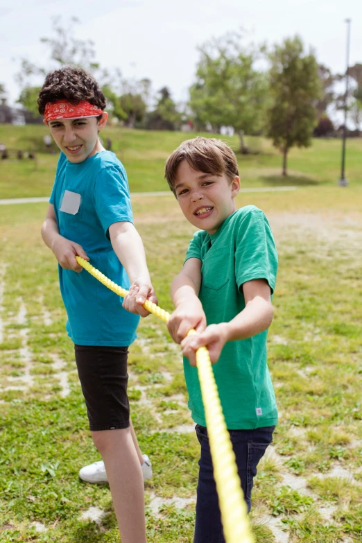 a couple of kids standing on top of a lush green field, yellow and blue ribbons, balance beams, playing games, bandanas
