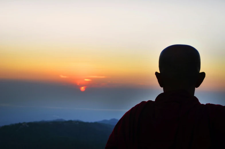 a person standing in front of a sunset, inspired by Shūbun Tenshō, pexels contest winner, portrait of monk, overlooking, myanmar, gazing off into the horizon