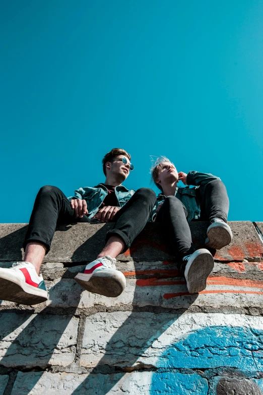 a couple of men sitting on top of a brick wall, trending on pexels, non-binary, high above the ground, concert, profile image
