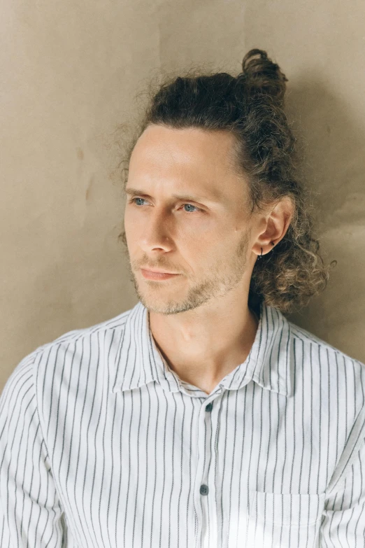 a man with a messy bun in his hair, an album cover, inspired by Daniël Mijtens, unsplash, renaissance, tom hiddleston, with long curly hair, casual pose, serious look