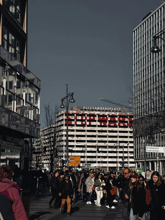 a crowd of people walking down a street next to tall buildings, a photo, pexels contest winner, berlin secession, billboard image, sovietwave aesthetic, sephora, seen from outside