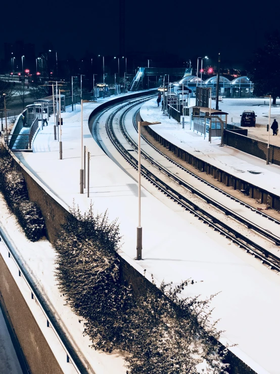 a train traveling down train tracks next to snow covered ground, by Jens Søndergaard, pexels contest winner, bus station, iphone photo, close to night, 🚿🗝📝