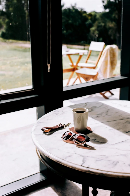 a table that has a cup of coffee on it, inspired by Elsa Bleda, trending on unsplash, visual art, sunglasses, french door window, sustainable materials, while marble