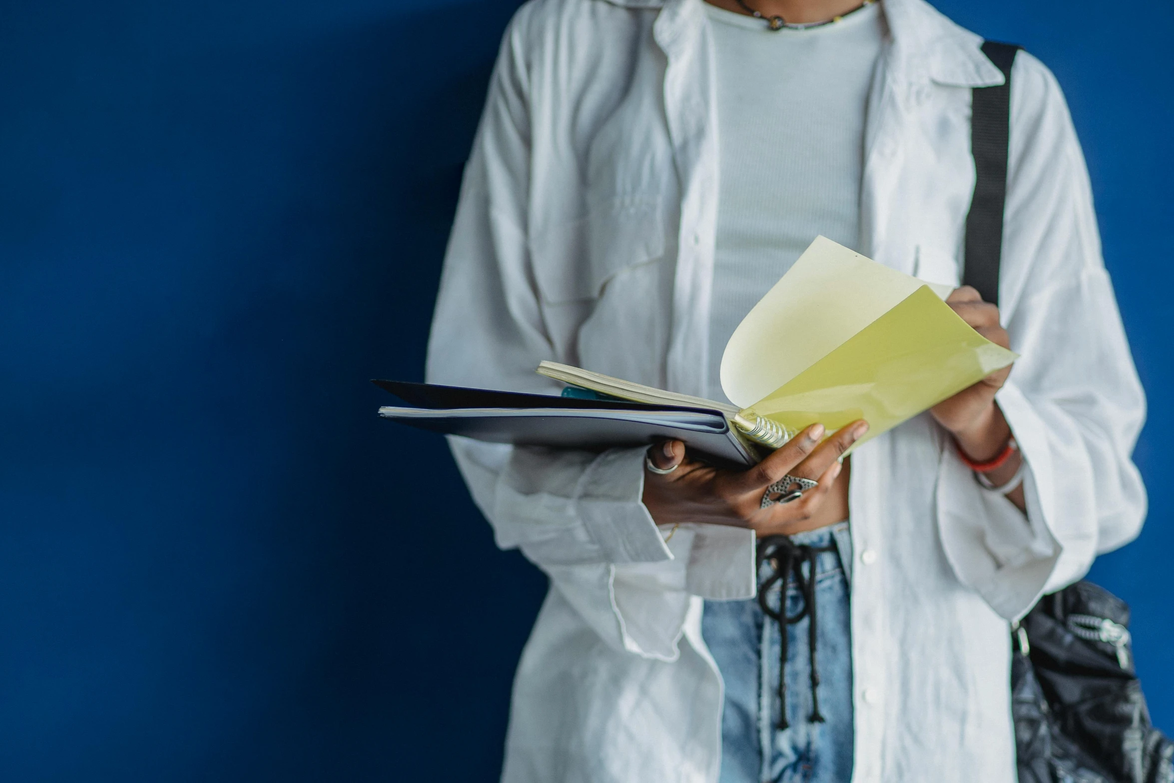 a woman standing in front of a blue wall holding a book, pexels contest winner, academic art, lab coat and tee shirt, yellowed paper, writing on a clipboard, layered paper