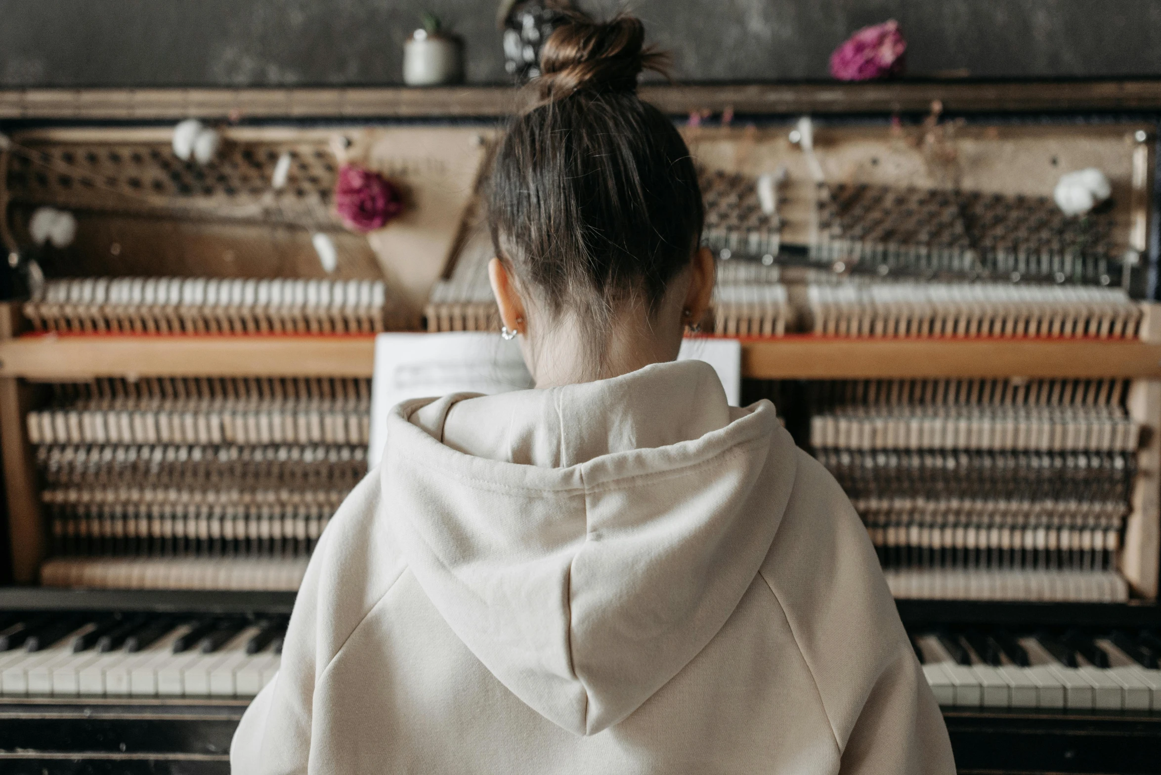 a woman sitting in front of a piano, trending on pexels, beige hoodie, rear-shot, nerdy music teacher with phd, cosy vibes