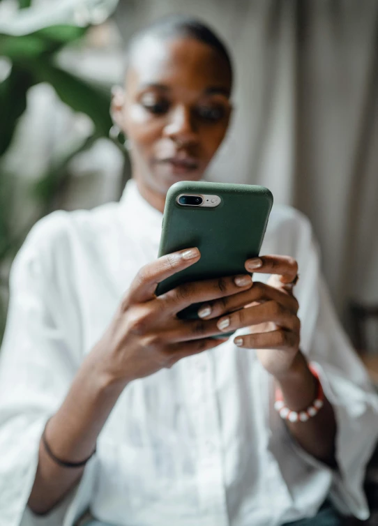 a woman sitting on a couch looking at her phone, trending on pexels, white shirt and green skirt, mkbhd, swedish, corporate phone app icon