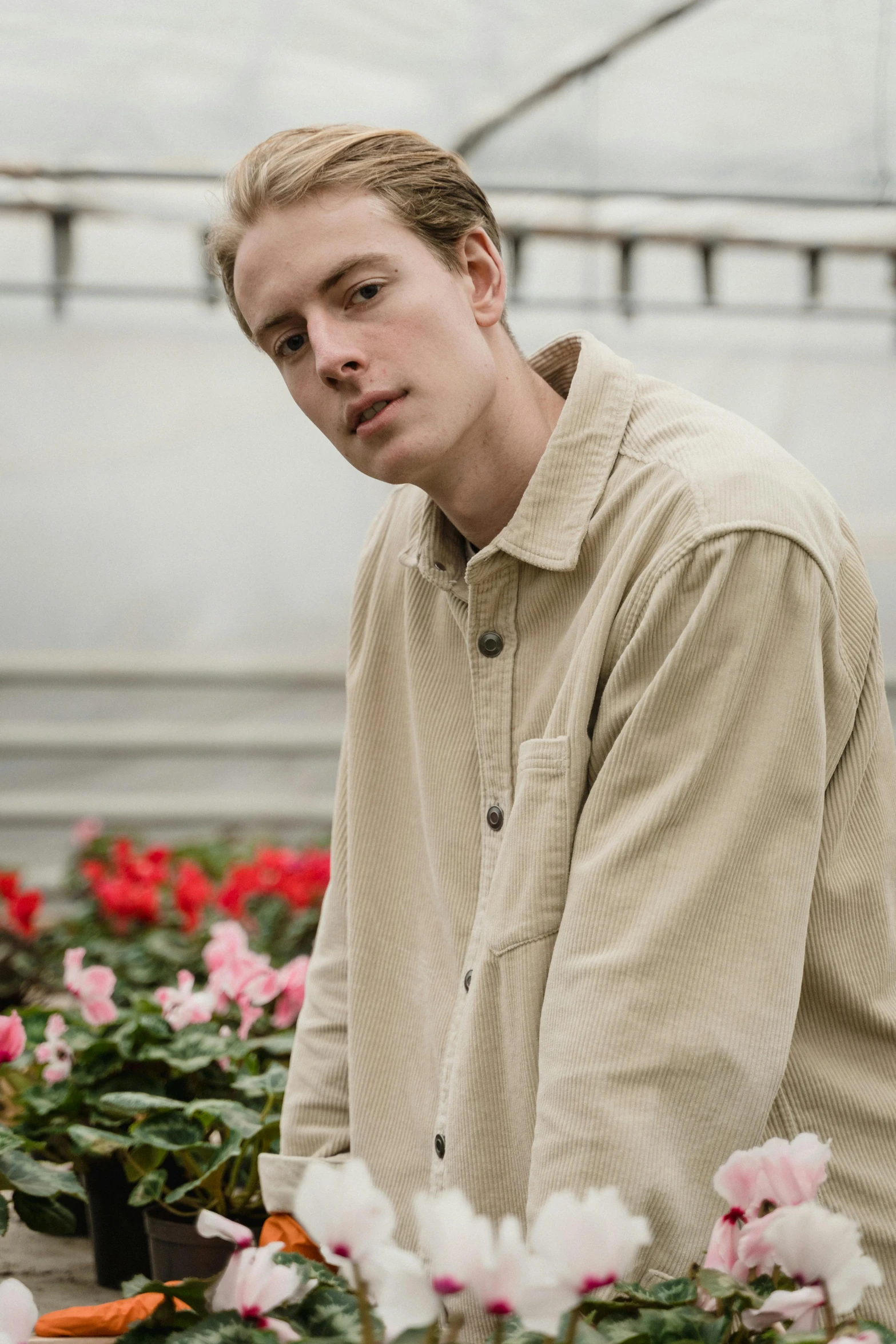 a man standing in a greenhouse surrounded by flowers, an album cover, inspired by Jesper Ejsing, trending on unsplash, renaissance, wear's beige shirt, thoughtful pose, corduroy, detail shot