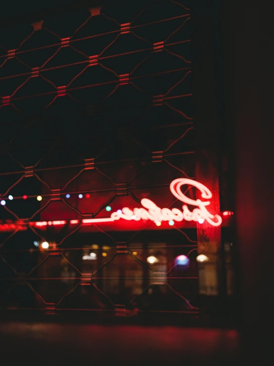 a red neon sign sitting on the side of a building, by Matt Cavotta, trending on unsplash, reflecting light in a nightclub, looking from side, cafe lighting, grainy