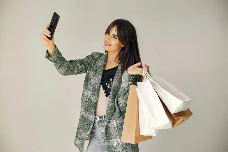 a woman taking a selfie with her cell phone, trending on pexels, people shopping, green and brown clothes, on grey background, wearing a fancy jacket