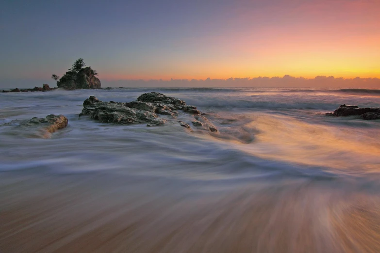 a large body of water sitting on top of a sandy beach, by Peter Churcher, unsplash contest winner, waves crashing at rocks, sunset panorama, bedhead, slow - shutter