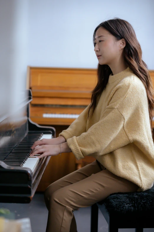 a woman sitting at a piano in a room, inspired by Song Xu, trending on pexels, wearing casual sweater, slight yellow hue, 奈良美智, performance