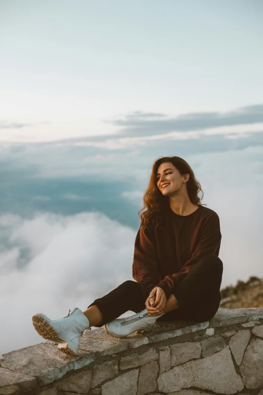 a woman sitting on top of a stone wall, happy clouds behind, portrait featured on unsplash, casual clothing, cloud jumper