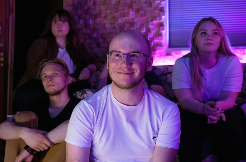 a group of people sitting next to each other, purple volumetric lighting, discord profile picture, liam brazier, relaxing and smiling at camera