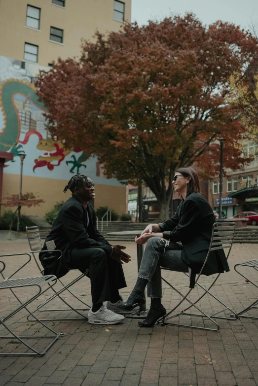 a couple of people that are sitting in chairs, an album cover, by Winona Nelson, pexels contest winner, street art, portland oregon, autumnal, looking at each other mindlessly, with black