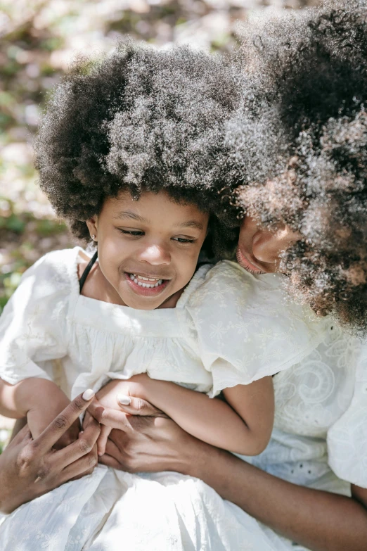 a couple of little girls sitting next to each other, an album cover, by Lily Delissa Joseph, pexels contest winner, natural hair, hugging and cradling, woman holding another woman, fluffy full of light