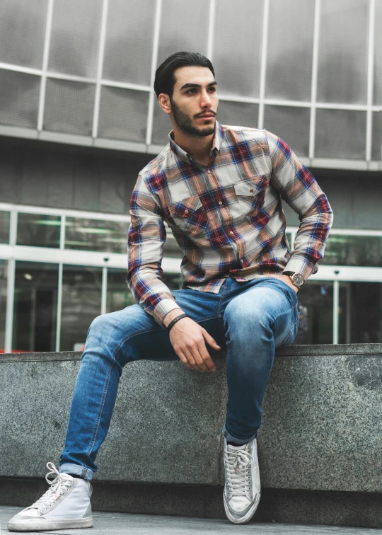 a man sitting on a ledge in front of a building, a colorized photo, trending on pexels, wearing a flannel shirt, ( ( ( wearing jeans ) ) ), amr elshamy, confident stance