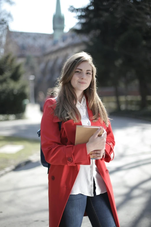 a woman in a red coat holding a book, at college, sanja stikovic, looking smart, slightly sunny