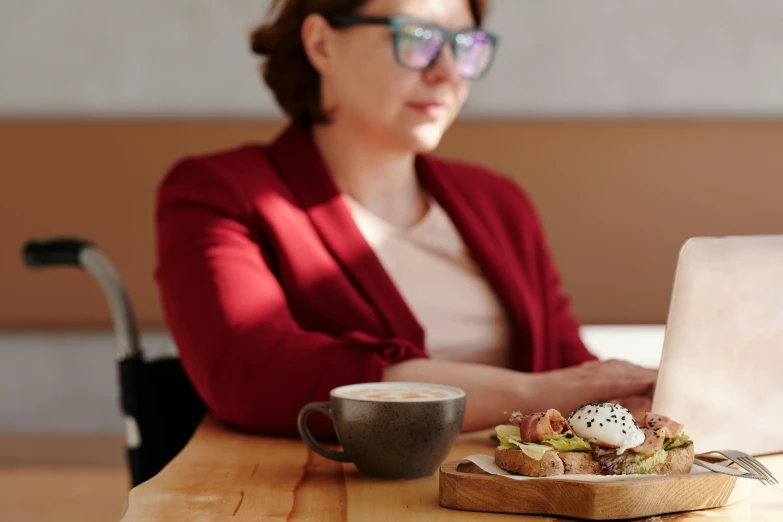 a woman sitting at a table in front of a laptop, by Carey Morris, trending on pexels, eggs benedict cumberbatch, on a wooden tray, wearing small round glasses, profile image