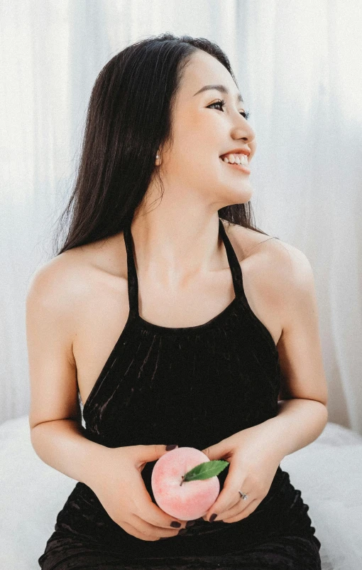 a woman sitting on a bed holding a piece of fruit, black halter top, holding a rose in a hand, jackie tsai style, headshot profile picture