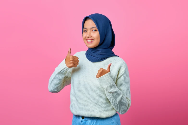 a woman wearing a hijab giving a thumbs up sign, inspired by Nazmi Ziya Güran, shutterstock contest winner, hurufiyya, pink and blue, plain background, casual pose, best practice