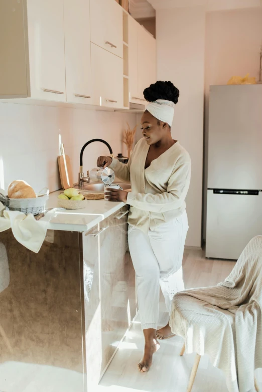 a woman in a bathrobe standing in a kitchen, by Arabella Rankin, pexels contest winner, black woman, tending on pinterest, brown and cream color scheme, full body image