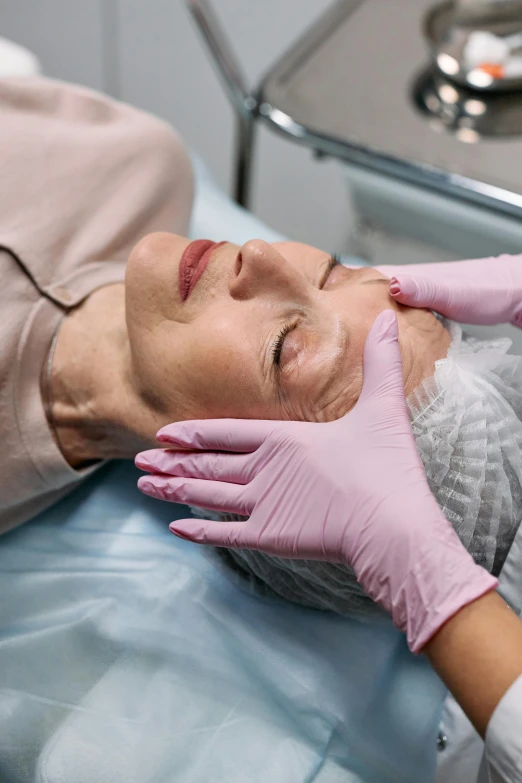 a close up of a person laying on a bed with gloves on, massurrealism, skincare, woman holding another woman, surgery, square facial structure