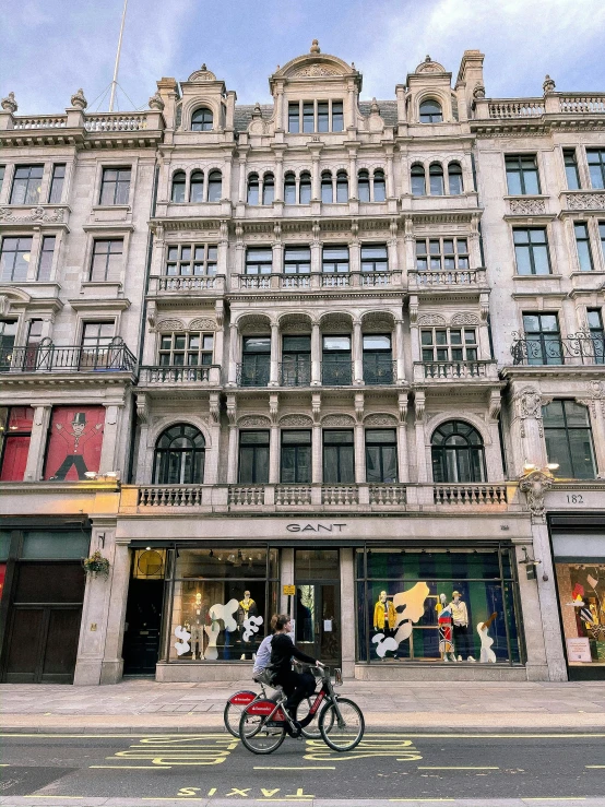 a person riding a bike in front of a building, shopwindows, in the center of the image, in london, giants