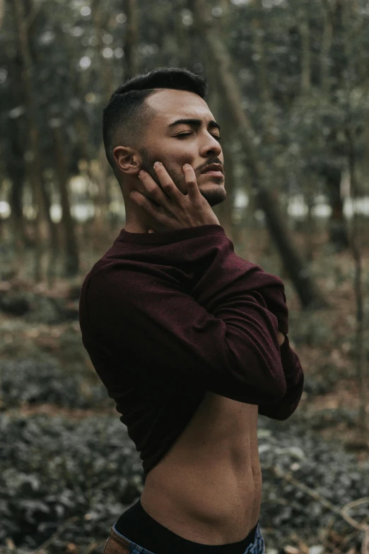 a man standing in the woods talking on a cell phone, an album cover, inspired by Byron Galvez, trending on pexels, model with attractive body, shaved sides, maroon, quiet beauty