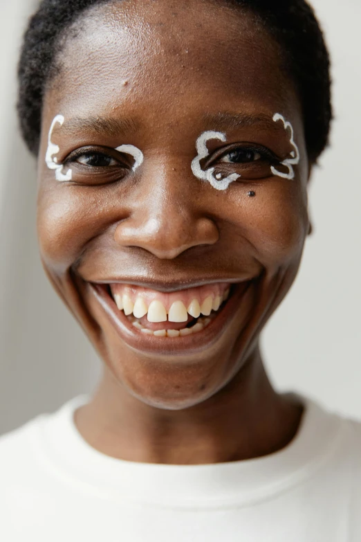 a smiling woman with eyeliners on her face, trending on pexels, afrofuturism, boy with neutral face, playful and cheerful, her face is coated in a white, wearing a patch over one eye