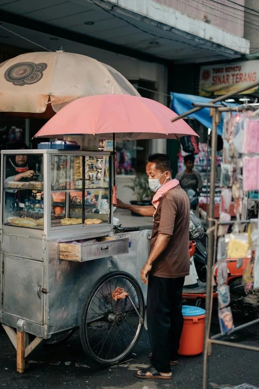 a man standing in front of a food cart, by Basuki Abdullah, trending on unsplash, single person with umbrella, pink, wearing facemask, square