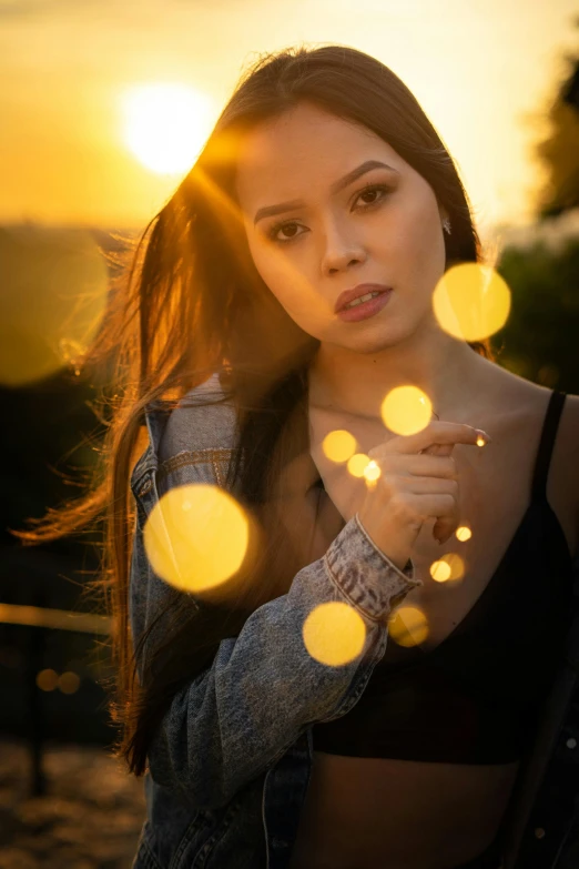a beautiful young woman standing in front of a sunset, by Robbie Trevino, art photography, glowing light orbs, close - up bokeh, modeling shoot, photograph taken in 2 0 2 0
