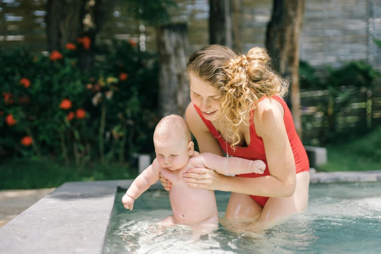 a woman in a red bathing suit holding a baby in a pool, pexels contest winner, bellybutton, caretaker, highly reflective, lane brown