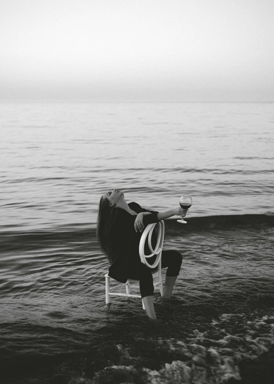 a chair sitting on top of a beach next to the ocean, a black and white photo, by Lucia Peka, pexels contest winner, surrealism, drinking, half face in the water, sittin, photograph ”