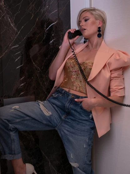 a woman sitting on a wall talking on a phone, an album cover, inspired by Elsa Bleda, trending on pexels, renaissance, wearing a pink tux, model エリサヘス s from acquamodels, jacket over bare torso, 1 9 8 0 s tech