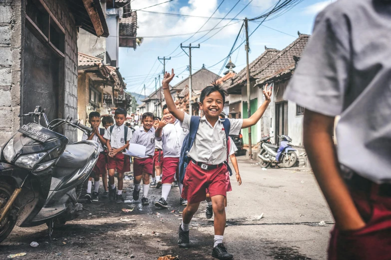 a group of young children walking down a street, a picture, pexels contest winner, happening, bali, waving arms, wearing a school uniform, background image