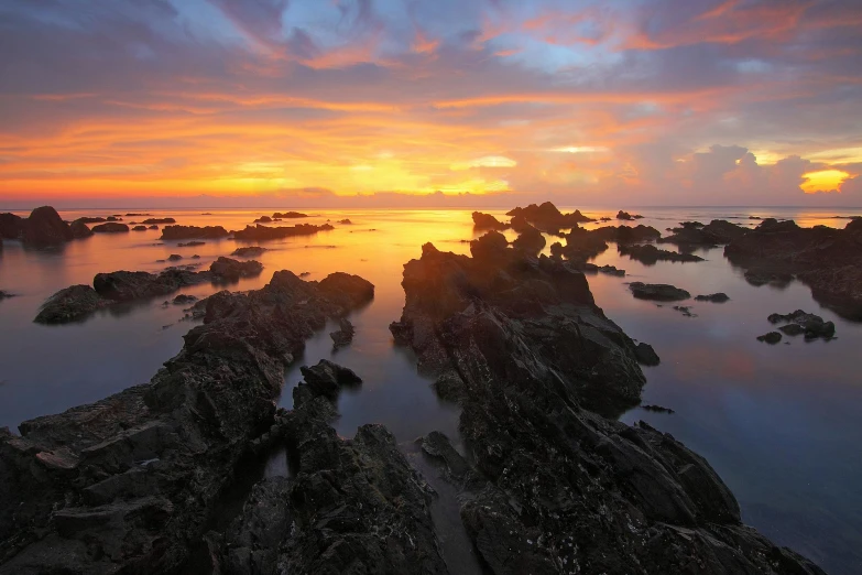 a sunset over a body of water with rocks in the foreground, quixel megascans, conde nast traveler photo