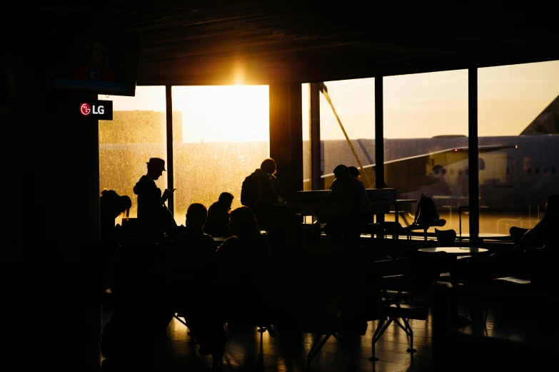 a group of people that are standing in front of a window, by Lee Loughridge, pexels contest winner, happening, hangar, warm sundown, people sitting at tables, black. airports