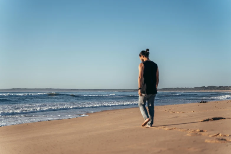 a man standing on a beach next to the ocean, pexels, aboriginal australian hipster, people walking into the horizon, wearing pants and a t-shirt, trailing off into the horizon