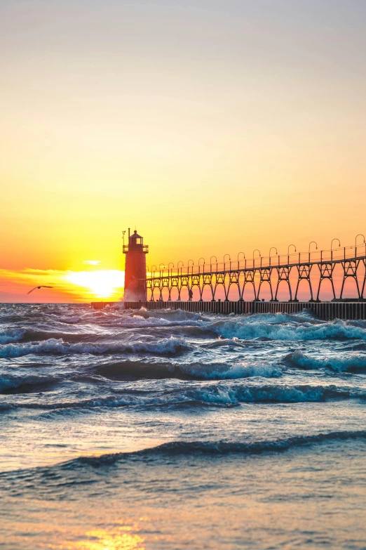 a lighthouse sitting on top of a beach next to the ocean, during a sunset, towering waves, michigan, festivals