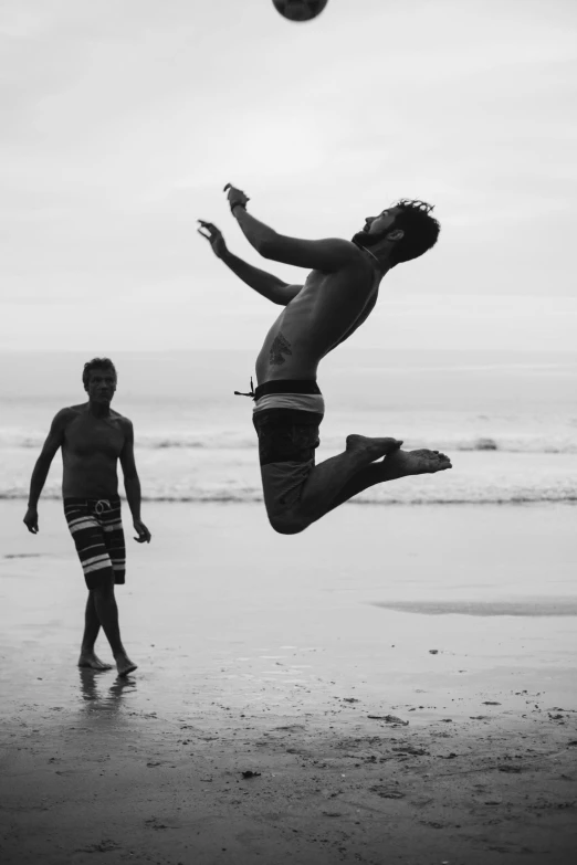 a man jumping in the air to catch a ball, a black and white photo, inspired by Garry Winogrand, pexels contest winner, arabesque, beach party, two male, happy people, capoeira