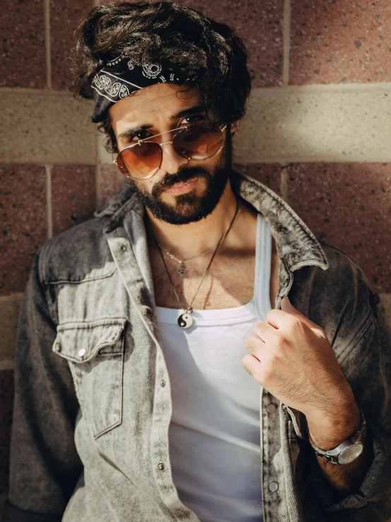 a man standing in front of a brick wall, an album cover, by Adam Dario Keel, trending on pexels, renaissance, wearing a bandana and chain, arab man light beard, non binary model, 7 0 s style