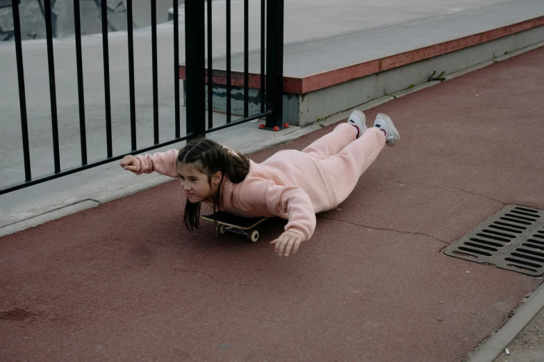 a little girl riding a skateboard down a sidewalk, by Emma Andijewska, she is laying on her back, wearing a tracksuit, pink body, dafne keen