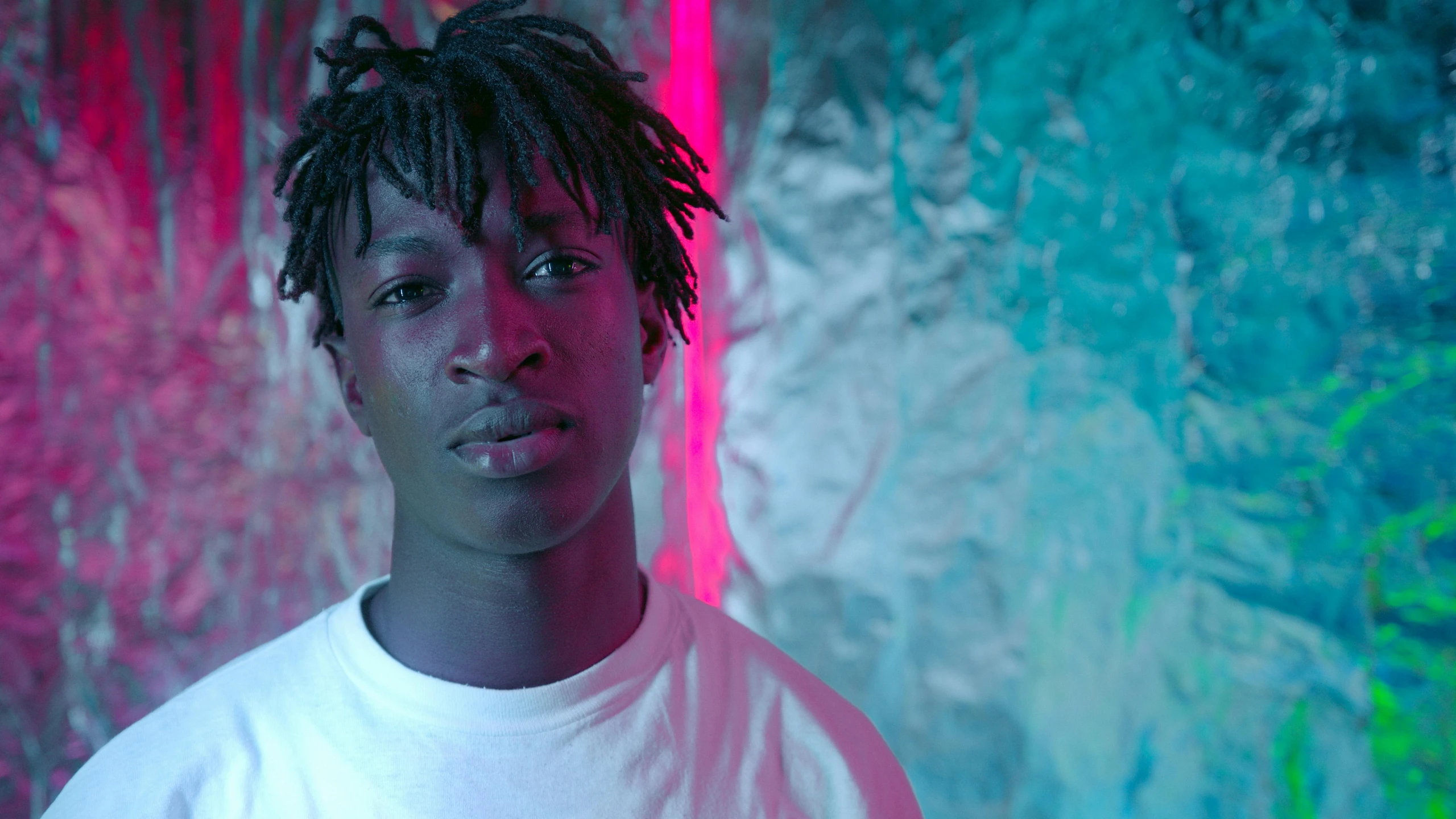 a man with dreadlocks standing in front of a wall, an album cover, pexels contest winner, hyperrealism, neon lighting medium full shot, black teenage boy, adut akech, finn wolfhard