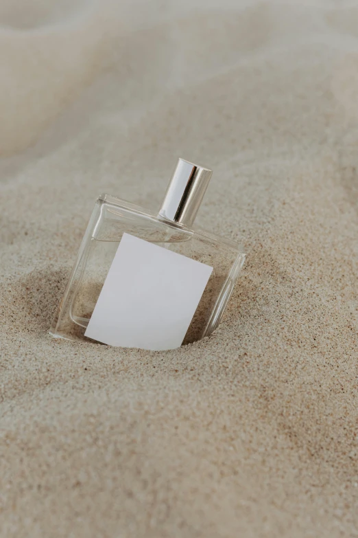 a bottle of perfume sitting in the sand, detailed product image, detail shot, paper, silver mist