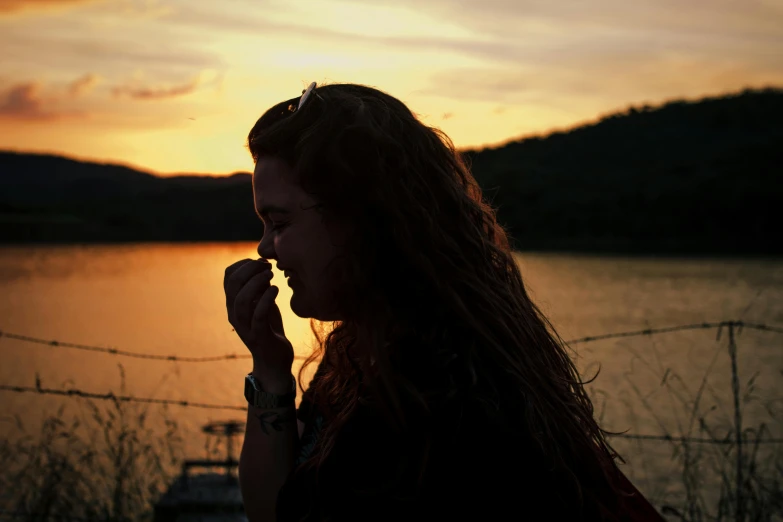 a woman standing in front of a body of water, inspired by Elsa Bleda, pexels contest winner, eating, backlit face, teenage girl, summer evening