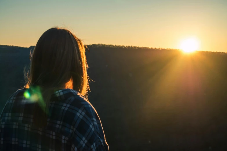 a woman standing on top of a mountain at sunset, by Lee Loughridge, pexels contest winner, backlit face, afternoon sunshine, facing away, full colour