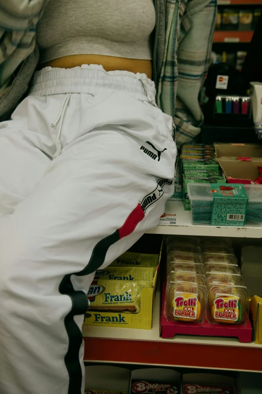 a woman leaning on a shelf in a store, by Nina Hamnett, flickr, wearing a tracksuit, snacks, close-up on legs, wearing a white gi